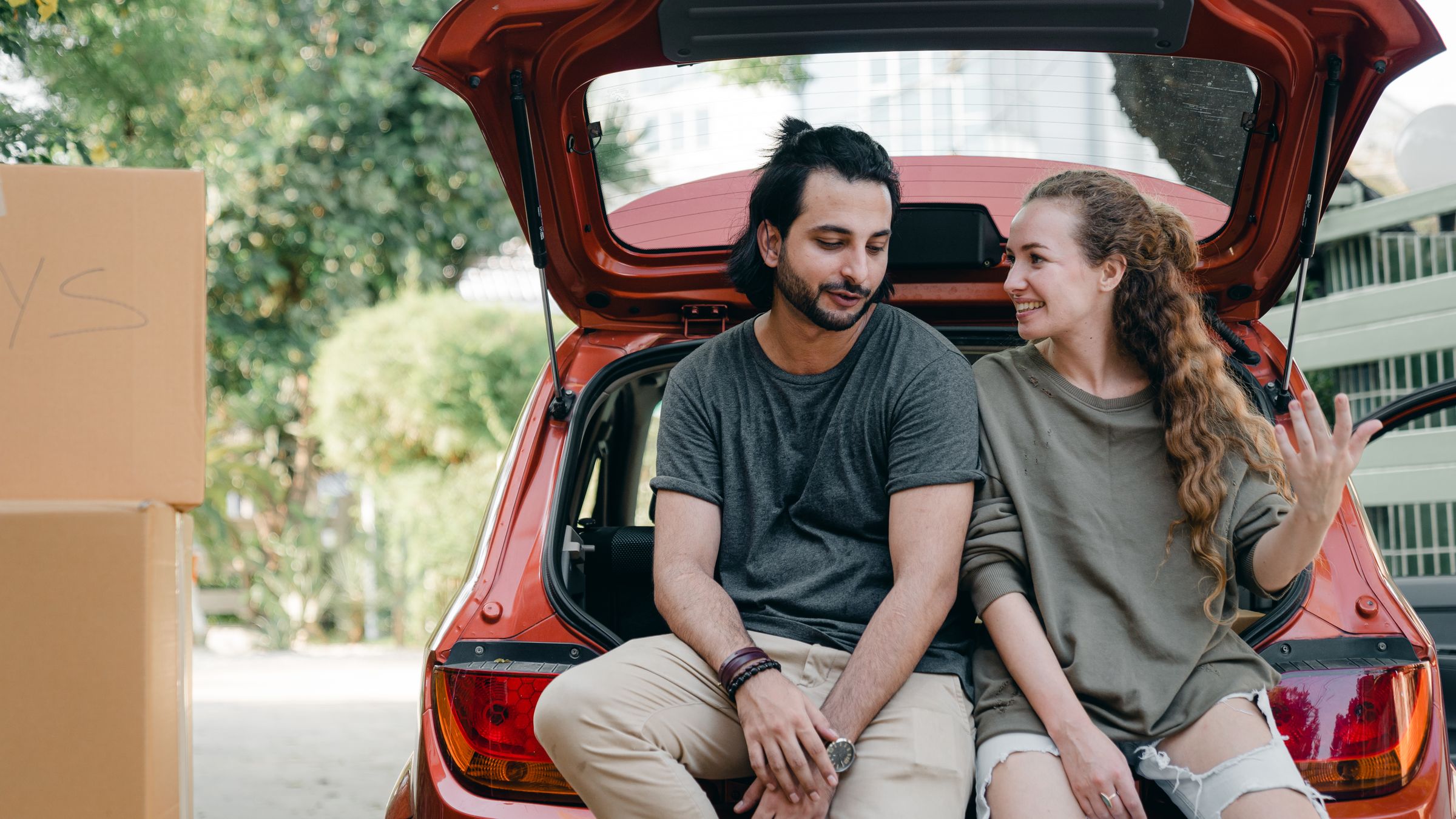 A couple sitting in the open boot of their car on moving day